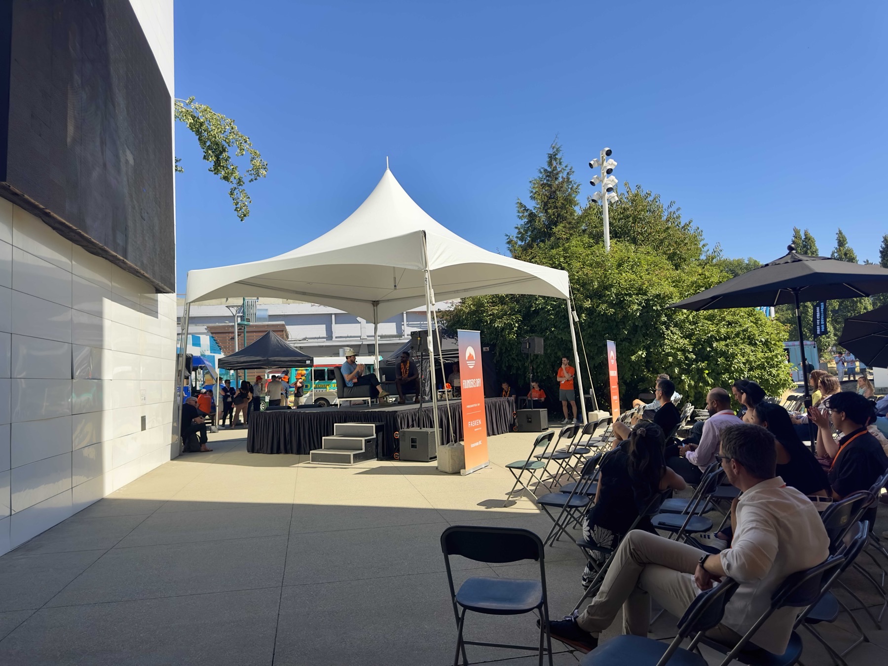 The Founders Day stage under a tent, front rows empty in the blaring sun while the seats in the shade fill up