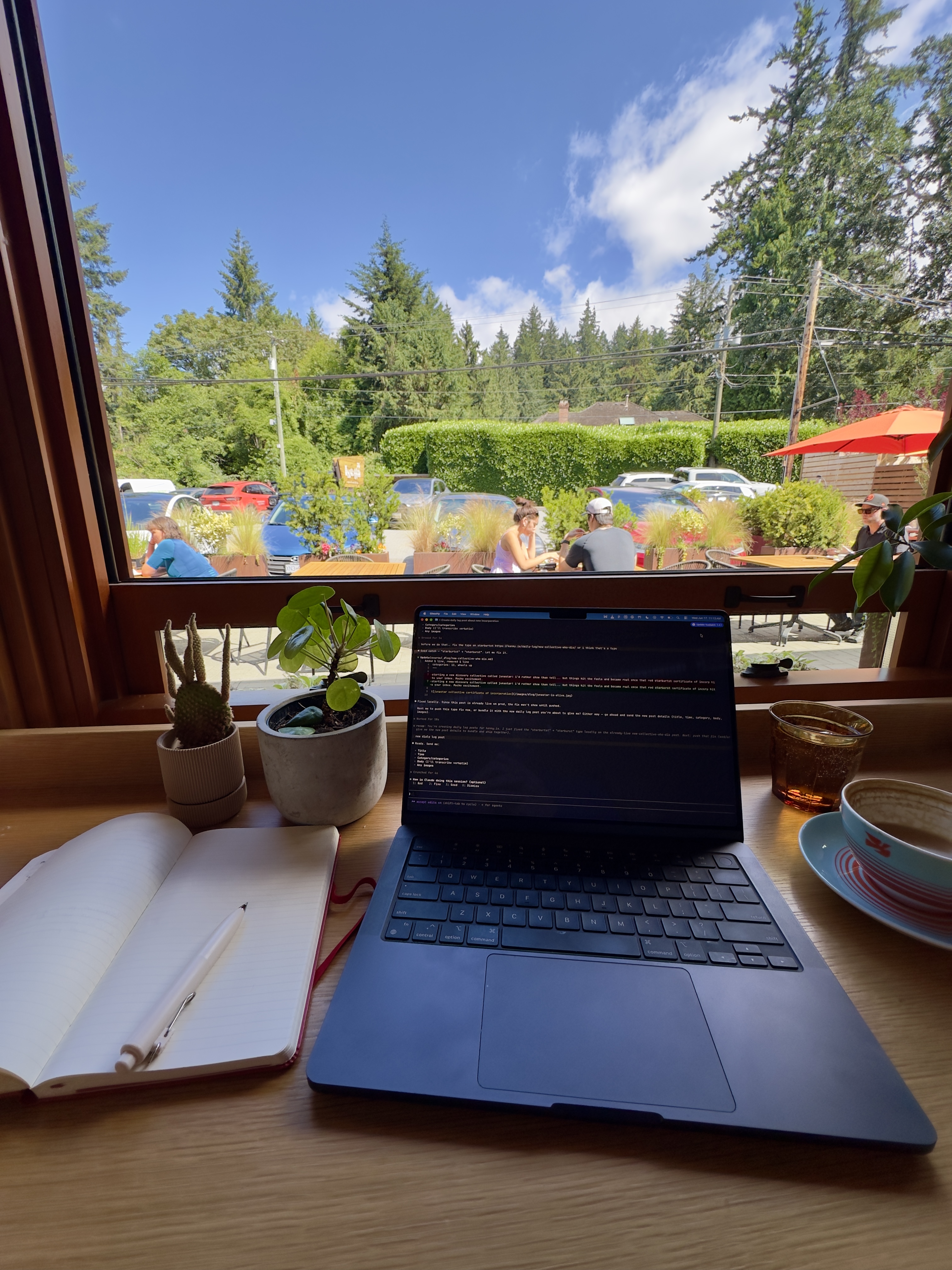 Laptop and open journal by a window with a forest view